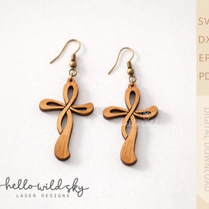 May include: A pair of wooden cross earrings with a unique, flowing design. The earrings are a light brown color and feature brass-colored ear wires. The words "hello wild sky" and "laser designs" are printed at the bottom of the image.