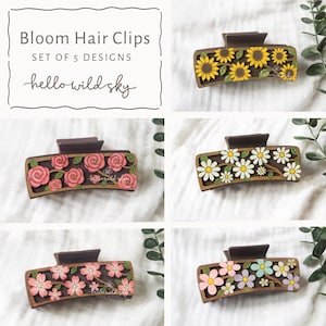 May include: A set of five rectangular hair clips featuring floral designs. Each clip has a dark brown base with layered wooden cutouts of sunflowers, roses, daisies, cherry blossoms, and mixed pastel flowers. Text reads Bloom Hair Clips.