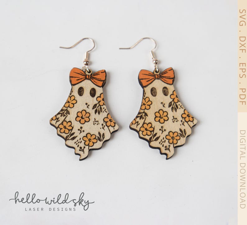 May include: A pair of wooden ghost earrings with orange bows and floral patterns. The earrings have silver hooks and are laser cut. The ghost-shaped earrings are decorated with orange flowers and leaves. The earrings are a digital download from Hello Wild Sky Laser Designs.