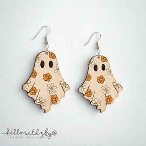 Könnte beinhalten: Ein Paar Holz-Geisterohrringe mit floralem Design. Die Ohrringe sind hellbraun mit orangefarbenen und weißen Blumen. Jeder Geist hat zwei schwarze Augen und einen silbernen Fischhaken. Der Text "hello wild sky" steht unten.