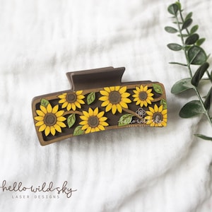 May include: A brown rectangular hair claw clip decorated with yellow sunflowers and green leaves. The clip has the text "hello wild sky laser designs". The clip is made of wood and is a digital download.