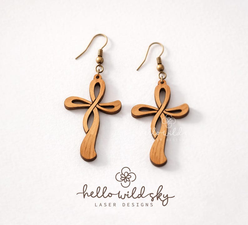 May include: A pair of wooden cross earrings with a unique, flowing design. The earrings are a light brown colour and feature brass-coloured ear wires. The logo "hello wild sky" is visible at the bottom.