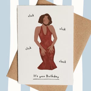 May include: Birthday card with an illustration of a person in a red dress, surrounded by the words "click" and "clack." The text "It's your Birthday" is at the bottom. The card is on a brown envelope, with a blue and white striped background.