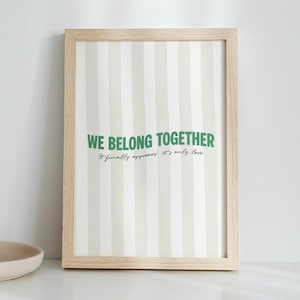 May include: A framed print with a light wood frame. The print has a striped background in white and green. The text "WE BELONG TOGETHER" is in green, with the smaller text "It finally appears, it's only love" below.