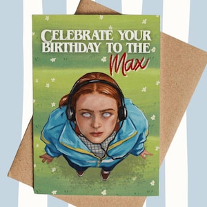 May include: Birthday greeting card featuring a person wearing headphones and a blue jacket, with the text "CELEBRATE YOUR BIRTHDAY TO THE MAX" in white and red. The card is on a brown envelope.