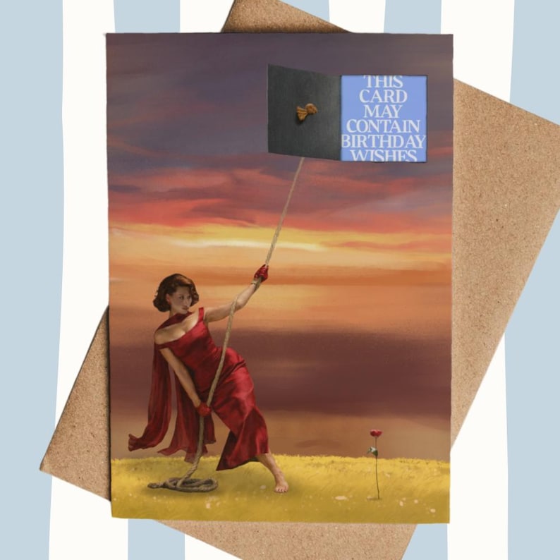 May include: Greeting card with a woman in a red dress pulling a rope attached to a black square with a gold bow. The card has the text "THIS CARD MAY CONTAIN BIRTHDAY WISHES" on a blue background. The background is a sunset.