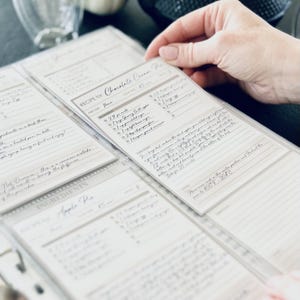 Personalized custom ring binder recipe book with hard cover and printed pages. Features recipe journal pages with sections for recipe name, prep time, cook time, servings, ingredients, directions, and notes. Includes 16 category dividers, 10 notes pages, 20 transparent sleeves, and one clear envelope sheet for small notes. Perfect for saving cherished meals, holiday dishes, and family traditions — a thoughtful gift for home cooks who love sharing meals together.