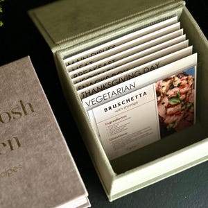May include: A light green recipe box with a hinged lid, filled with recipe cards. The cards are labeled with categories like "Main Dishes" and "Vegetarian." One card features a photo of bruschetta with shrimp.