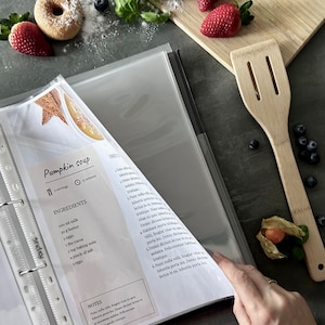 Personalized custom ring binder recipe book with hard cover and printed pages. Features recipe journal pages with sections for recipe name, prep time, cook time, servings, ingredients, directions, and notes. Includes 16 category dividers, 10 notes pages, 20 transparent sleeves, and one clear envelope sheet for small notes. Perfect for saving cherished meals, holiday dishes, and family traditions — a thoughtful gift for home cooks who love sharing meals together.