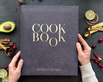 May include: A dark gray cookbook with the words "COOK BOOK" in gold lettering on the front cover. The text "Steffany's Recipes" is also in gold lettering on the front cover.