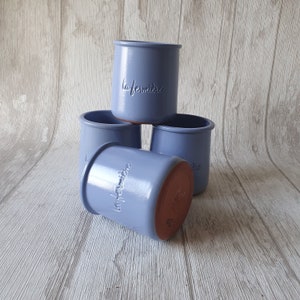 Op de afbeelding: Vier blauwe keramische potten met de tekst "la fermiere" in reliëf aan de zijkant. De potten zijn op elkaar gestapeld.