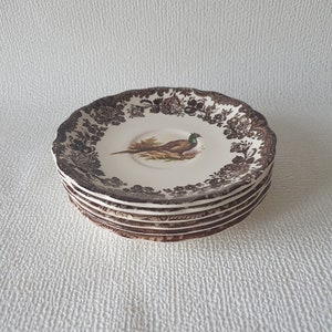 Può includere: Una pila di sei tazze da tè in ceramica marrone e bianca con un motivo di fagiano. Le tazze hanno un bordo ondulato e un motivo floreale.