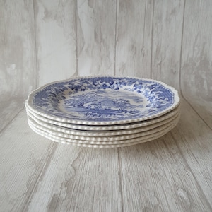May include: A stack of six white ceramic dinner plates with a blue and white floral pattern. The plates have a scalloped edge and a beaded rim.