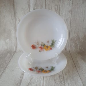May include: Two white ceramic bowls with a floral design. The bowls have a white background with a cluster of orange, yellow, and white flowers.