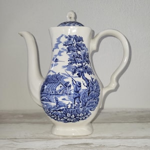 Może przedstawiać: Zestaw trzech ceramicznych kubków z nakrapianym, matowym wykończeniem. Kubki są w odcieniach kremu, jasnoszarym i ciemnoszarym. Każdy kubek ma prosty, minimalistyczny design i zaokrąglony uchwyt.