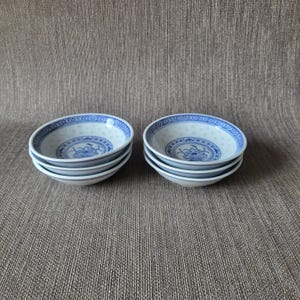 Peut inclure: Deux ensembles de quatre petits bols en porcelaine blanche avec des motifs floraux et géométriques bleus. Les bols présentent un motif ajouré délicat sur le bord et un motif floral central. Les bols sont empilés.