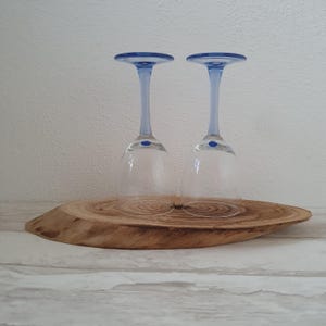 Op de afbeelding: Twee heldere glazen wijnglazen met blauwe randen en bodems die op een houten onderzetter staan.