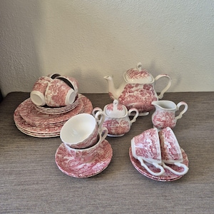 Könnte beinhalten: Ein komplettes Vintage-Teeservice in einem rot-weißen Toile-Muster. Das Set umfasst eine Teekanne, eine Zuckerdose, einen Sahnekännchen, Tassen, Untertassen und Teller. Das Teeservice ist auf einer neutralen Oberfläche angeordnet.