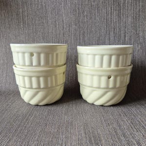 May include: Two stacks of two cream-colored ceramic ramekins, totaling four individual bowls. Each ramekin features a smooth, glossy finish with vertical fluted detailing on the upper half and a subtle diagonal twisted pattern on the lower base.