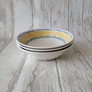 May include: Three white ceramic bowls with a yellow, green, and blue rim design. The bowls are stacked on top of each other.