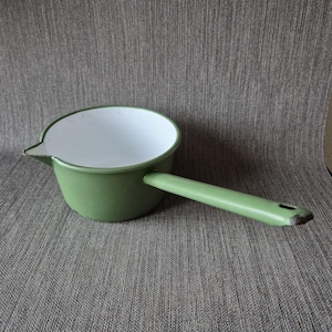 May include: A small, green enamel saucepan with a long handle and a pouring spout. The interior is white, and the handle has a hole at the end. The pan is designed for cooking and is likely vintage.