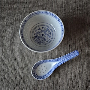 May include: A white ceramic bowl and matching spoon featuring blue dragon motifs and translucent rice grain patterns. The bowl has a blue geometric rim, while the spoon handle displays a blue cross-hatch pattern and the bowl of the spoon has dots.