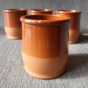 May include: Four ceramic cups with a two-tone design. The upper part is a rich, warm brown, while the lower section is a lighter, tan colour. The cups have a simple, cylindrical shape and a smooth, glossy finish. The cups are likely for drinking.