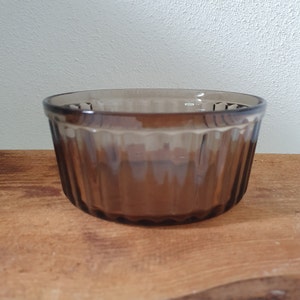 Könnte beinhalten: Eine braune Glasschüssel mit geriffeltem Design. Die Schüssel ist leer und steht auf einer Holzoberfläche.