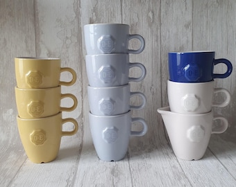 Tasses à café et crémier de différentes couleurs de Douwe Egberts Holland avec le sceau de la marque Douwe Egberts en relief, design de Nikolai Carels