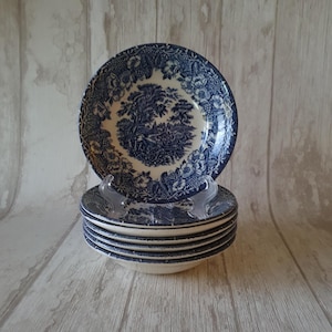 May include: A stack of six blue and white ceramic bowls with a floral pattern. The bowls have a white background with a blue floral design and a blue scene of a forest with a river.