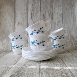 Puede incluir: Juego de seis tazas de té y platillos blancos con un patrón floral azul. Las tazas y los platillos están apilados uno encima del otro.