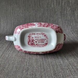 May include: An antique white and red gravy boat with a detailed pattern. The bottom of the boat features the text "THE HUNTER by MYOTT HAND ENGRAVED PERMANENT COLOURS MADE IN ENGLAND".