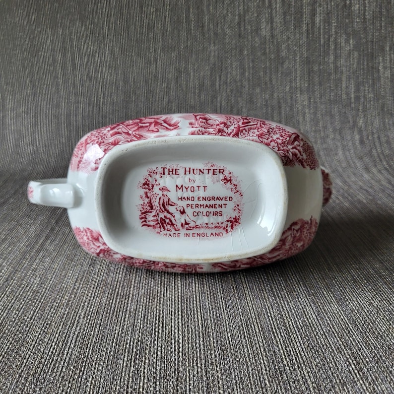 May include: An antique white and red gravy boat with a detailed pattern. The bottom of the boat features the text "THE HUNTER by MYOTT HAND ENGRAVED PERMANENT COLOURS MADE IN ENGLAND".