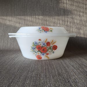 Op de afbeelding: Witte ovenschaal met een doorzichtig deksel. De schaal is versierd met een bloemenpatroon met rode klaprozen, blauwe bloemen en tarwearen. De schaal heeft een rechthoekige vorm met afgeronde randen en een doorzichtig plastic deksel.