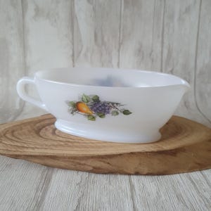 Puede incluir: Salsera de cerámica blanca con un diseño de pera y uvas. La salsera tiene una asa en el lado izquierdo y un pico en el lado derecho.