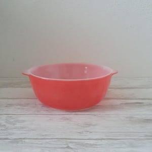 Op de afbeelding: Een roze en oranje glazen mengkom met twee handvatten. De kom is van Pyrex en is in goede staat.