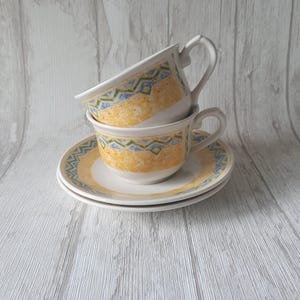 May include: Two yellow and blue patterned teacups stacked on top of each other with a matching saucer underneath.