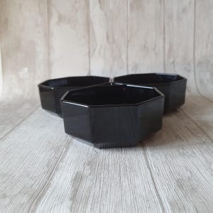 Peut inclure: Trois bols en verre octogonaux noirs. Les bols sont disposés en forme de triangle, le bol avant étant en focus.