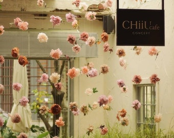May include: A cafe sign with the text "CHiiL cafe CONCEPT" hanging from the ceiling. The sign is black with gold lettering. The cafe is decorated with a string of pink and white paper flowers.