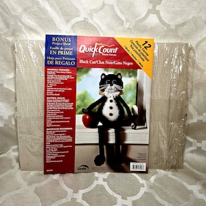 May include: A Quick Count plastic canvas kit with a black cat design. The kit includes 12 plastic canvases and a project sheet. The cat is black and white, holding a red apple.