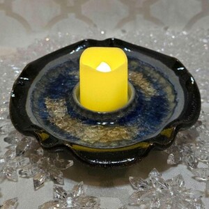 Peut inclure: Un bougeoir en céramique bleu et noir avec un bord ondulé. Une bougie jaune est placée au centre du bougeoir.