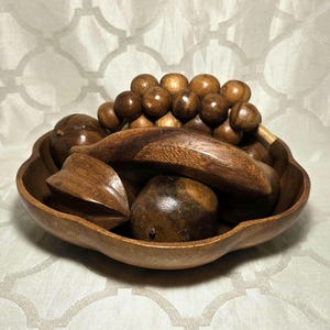 Op de afbeelding: Een houten kom gevuld met houten fruit. De kom heeft een geschulpte rand en bevat houten druiven, peren en ander fruit. Het hout heeft een warme, bruine tint.