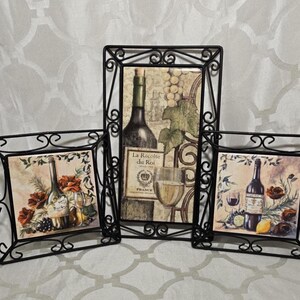 May include: Three framed tile wall decor pieces with a wine theme. Each tile features a different image of wine bottles, grapes, and glasses. The frames are black metal with a scrolled design.