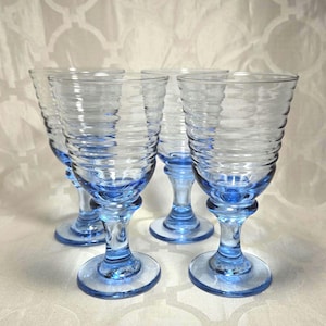 Op de afbeelding: Set van vier blauwe glazen wijnglazen met een geribbeld ontwerp. De glazen hebben een helder lichaam en een blauwe basis.