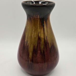 Peut inclure: Un petit vase en céramique brun, rouge et or avec un sommet évasé et un fond arrondi.
