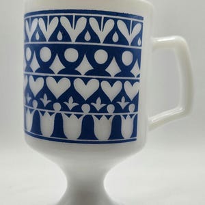 Peut inclure: Une tasse en céramique blanche avec un motif géométrique bleu et blanc. La tasse a une base en piédestal.