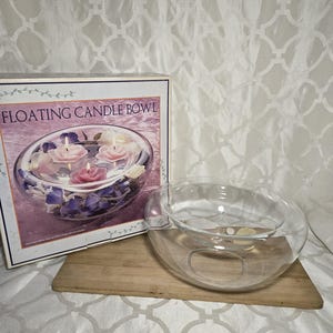 May include: A clear glass floating candle bowl with a box that reads "FLOATING CANDLE BOWL". The bowl is on a wooden board. The box shows the bowl with floating candles and flowers.