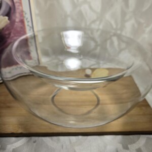 May include: A clear glass serving bowl with a unique, curved design. The bowl sits on a wooden surface, showcasing its elegant shape. The bowl has a circular base and a wider, open top, perfect for serving salads or displaying decorative items.