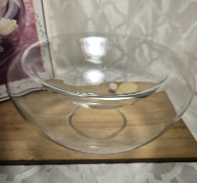 May include: A clear glass serving bowl with a unique, curved design. The bowl sits on a wooden surface, showcasing its elegant shape. The bowl has a circular base and a wider, open top, perfect for serving salads or displaying decorative items.