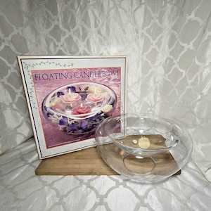 May include: A clear glass floating candle bowl with a box that reads "FLOATING CANDLE BOWL". The box shows the bowl with floating candles and floral accents. The bowl sits on a wooden board.